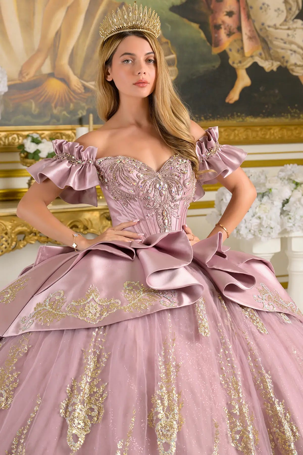 Woman in a mauve gown with gold details and a tiara, standing in an ornate room.