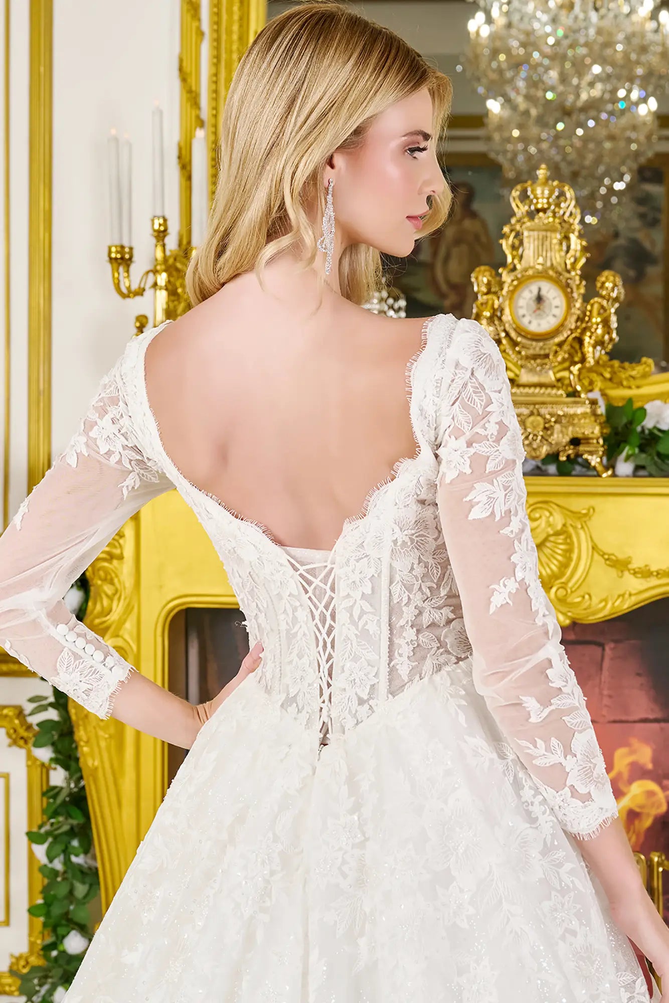 Woman wearing a wedding gown with corset closure, sheer sleeves, and flowing train