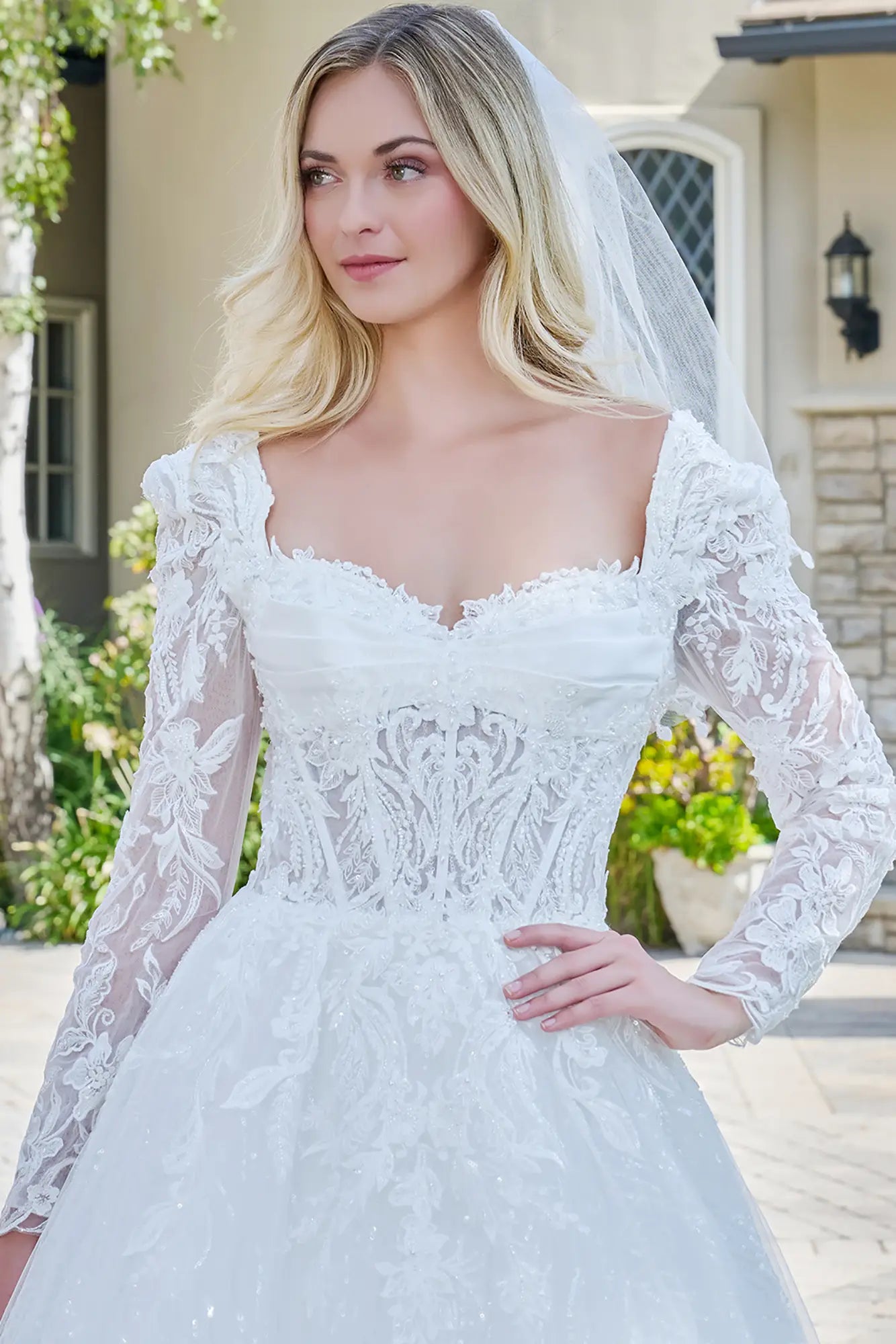 Woman wearing a white lace wedding dress with long sleeves outdoors.
