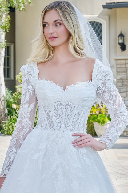 Woman wearing a white lace wedding dress with long sleeves outdoors.