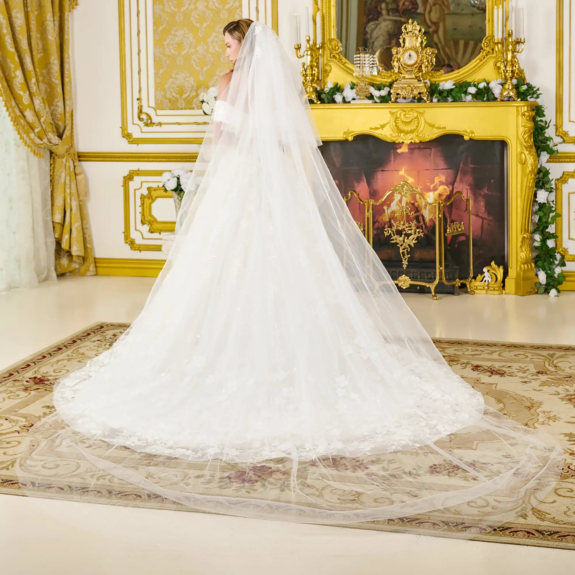 White wedding dress with a long train in a luxurious room with gold decor and a fireplace.