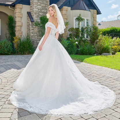 Woman in a white wedding dress standing on a driveway with a house and garden in the background