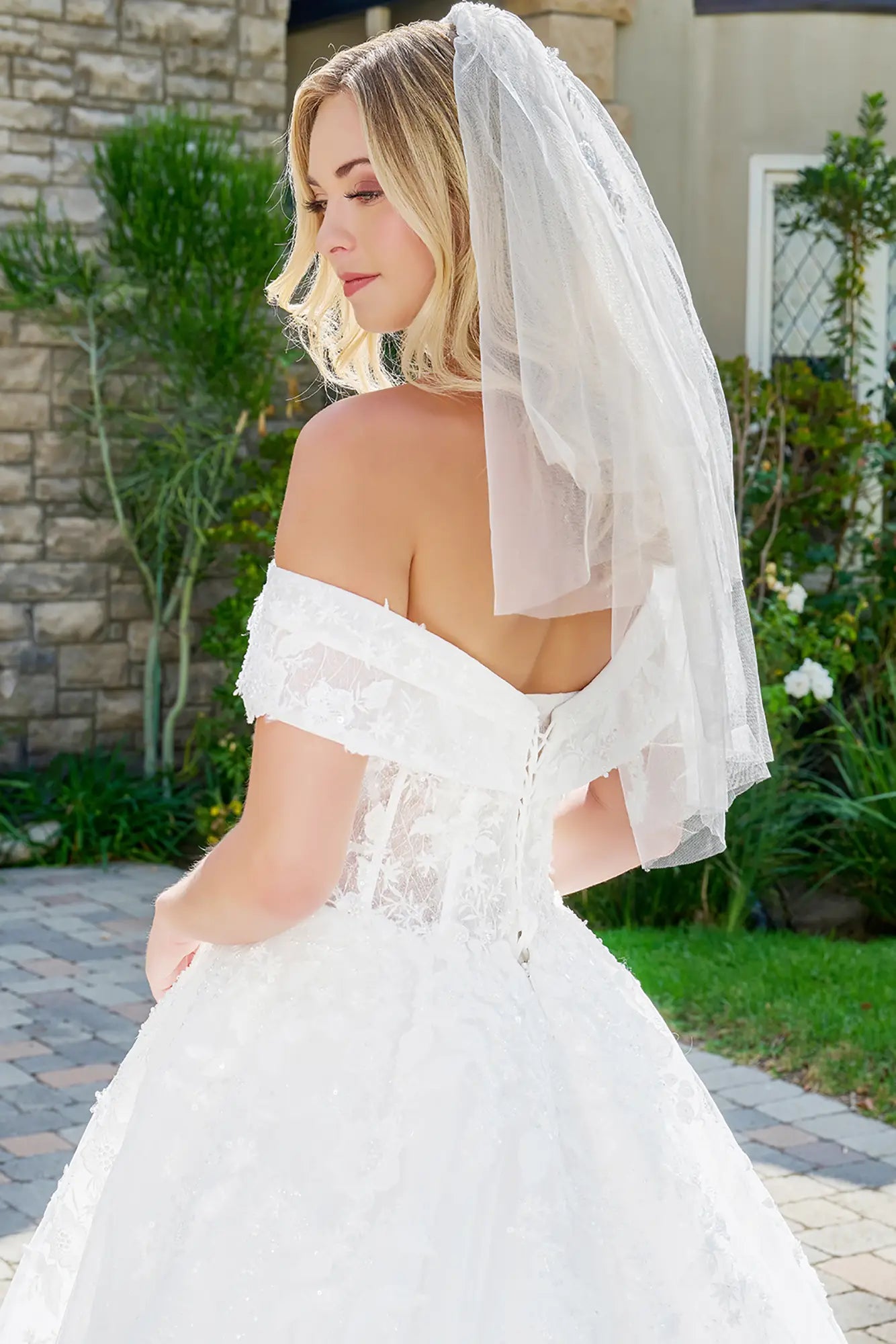 Woman in a white wedding dress with a veil standing outdoors.