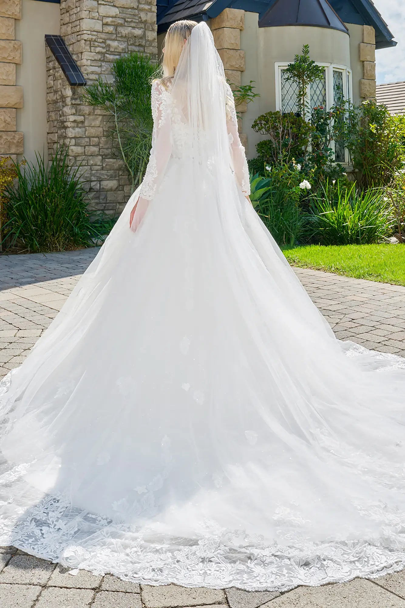 White wedding dress with a long train on a paved driveway.
