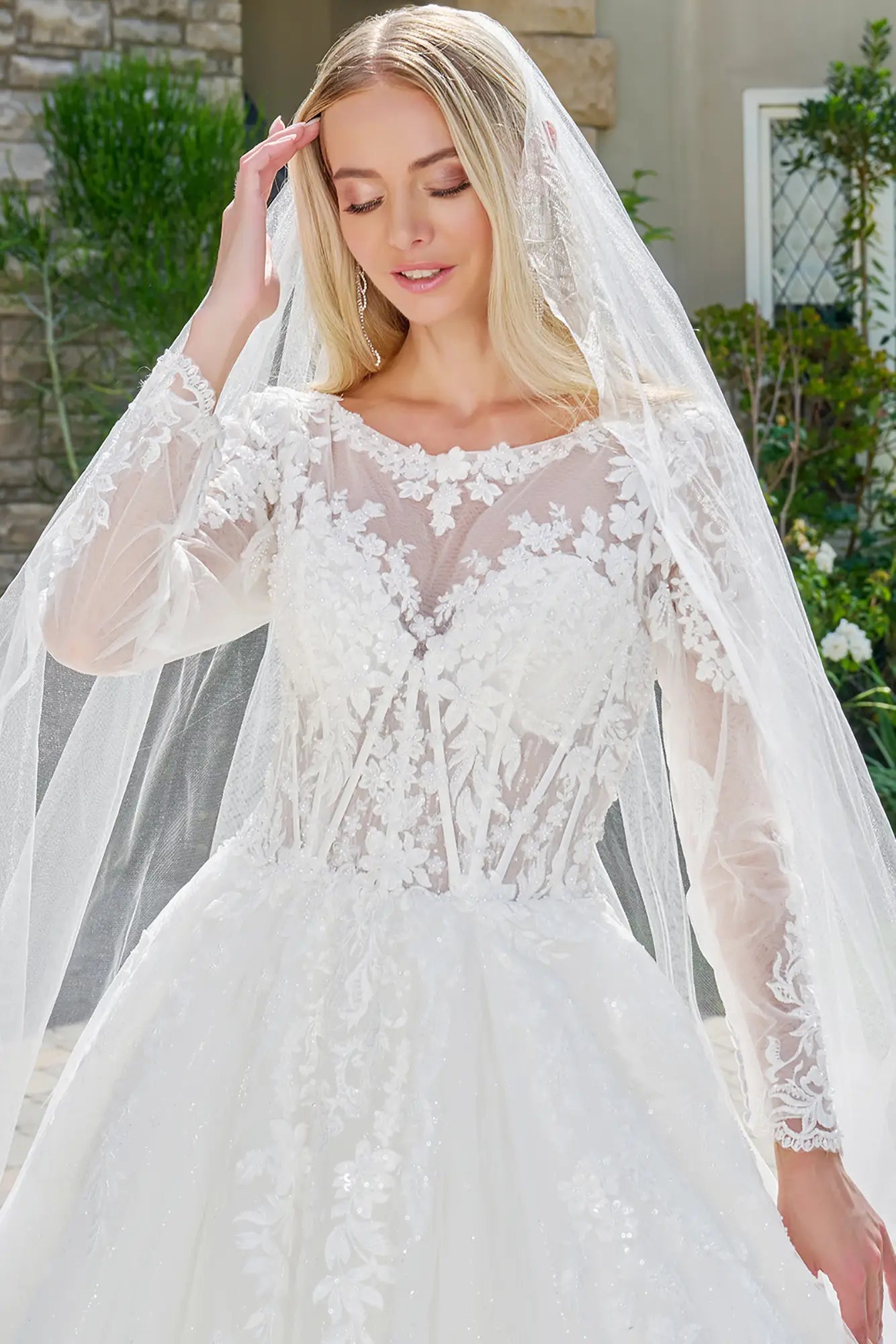 Woman wearing a white wedding dress with long sleeves and a veil outdoors.
