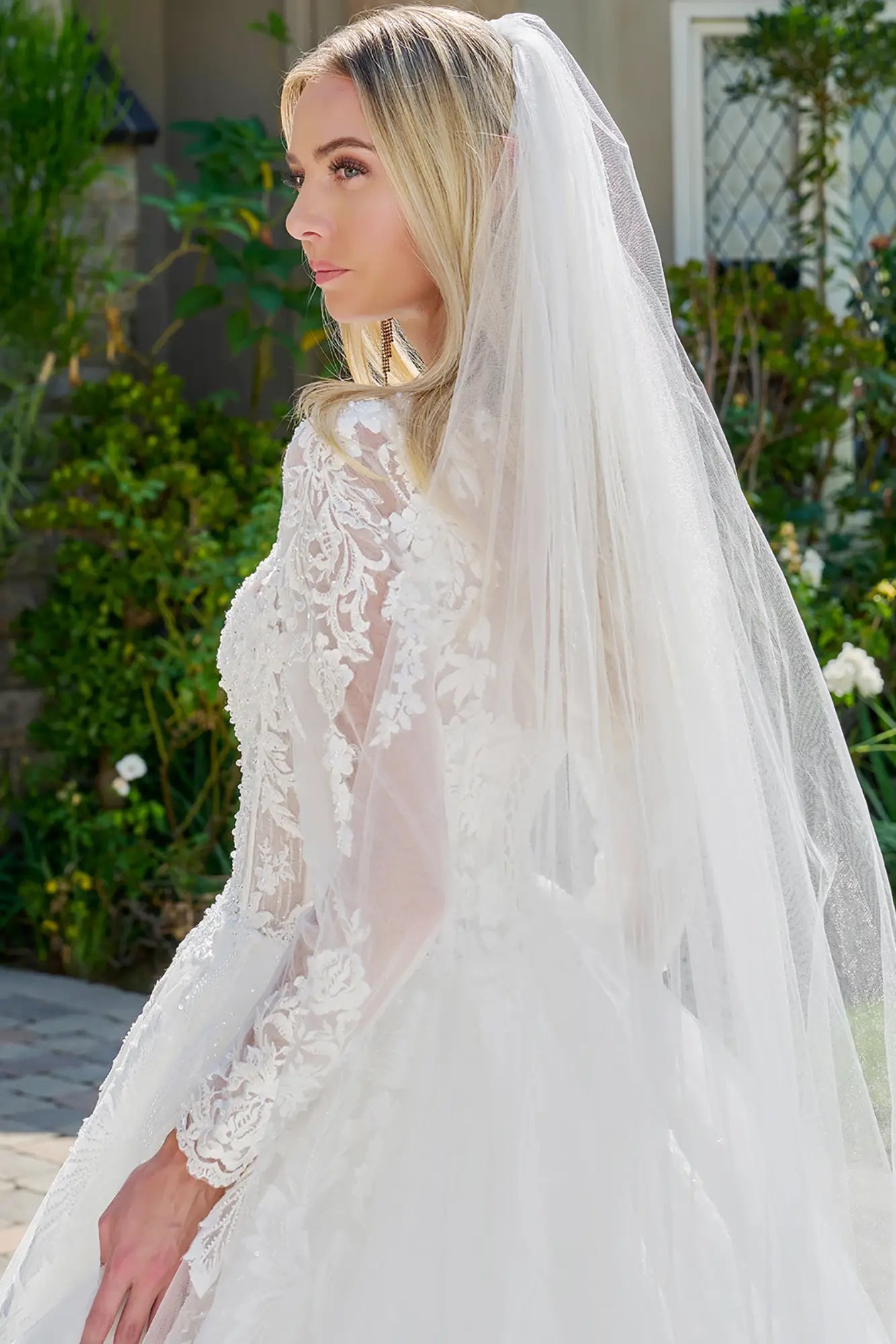 Woman wearing a white wedding dress with a long veil outdoors.