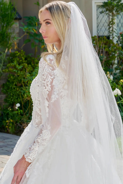 Woman wearing a white wedding dress with a long veil outdoors.