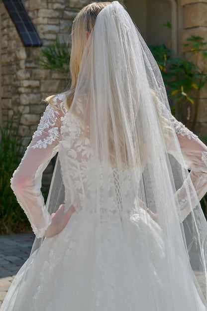 Person wearing a white lace wedding dress with a long veil outdoors.