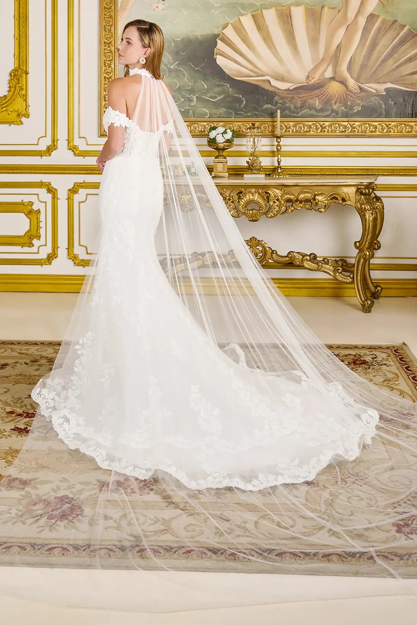 Woman in a white wedding dress with a long veil standing in an ornate room.