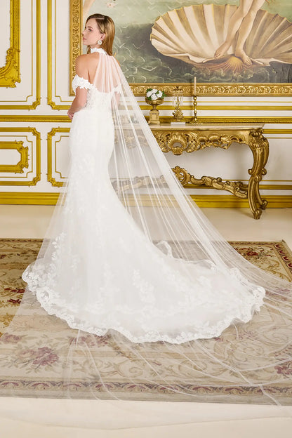 Woman in a white wedding dress with a long veil standing in an ornate room.