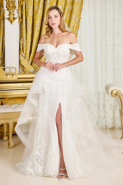 Woman wearing a white off-shoulder wedding dress with a high slit in a decorated room.