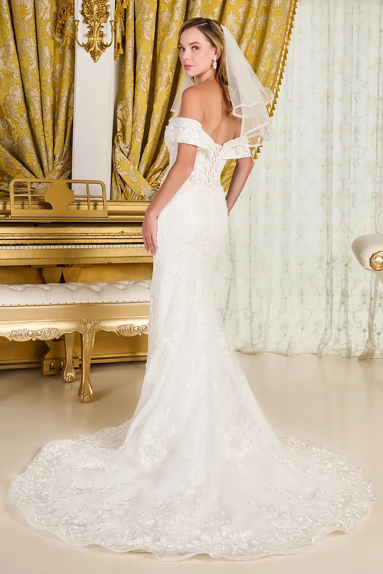 Woman in a white wedding dress standing in an opulent room with gold curtains and a piano.