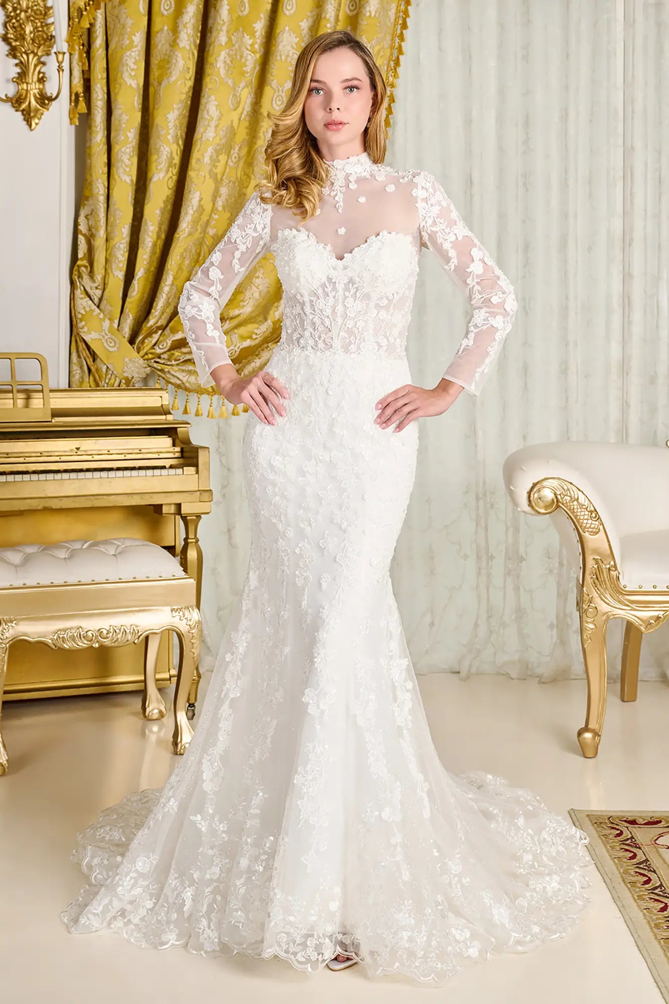 Woman in a white lace wedding dress standing in an elegant room with gold curtains and furniture.
