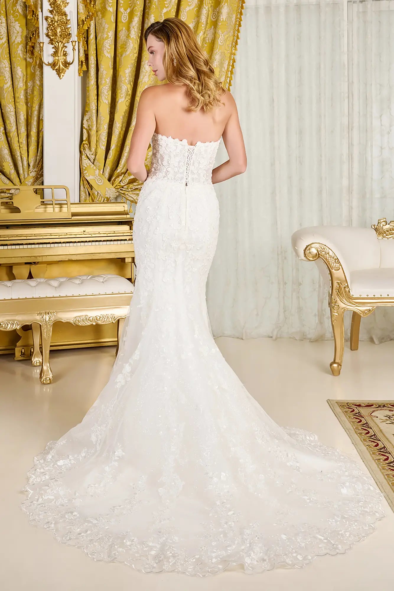 Woman in a white strapless gown standing in an opulent room with gold curtains and furniture.