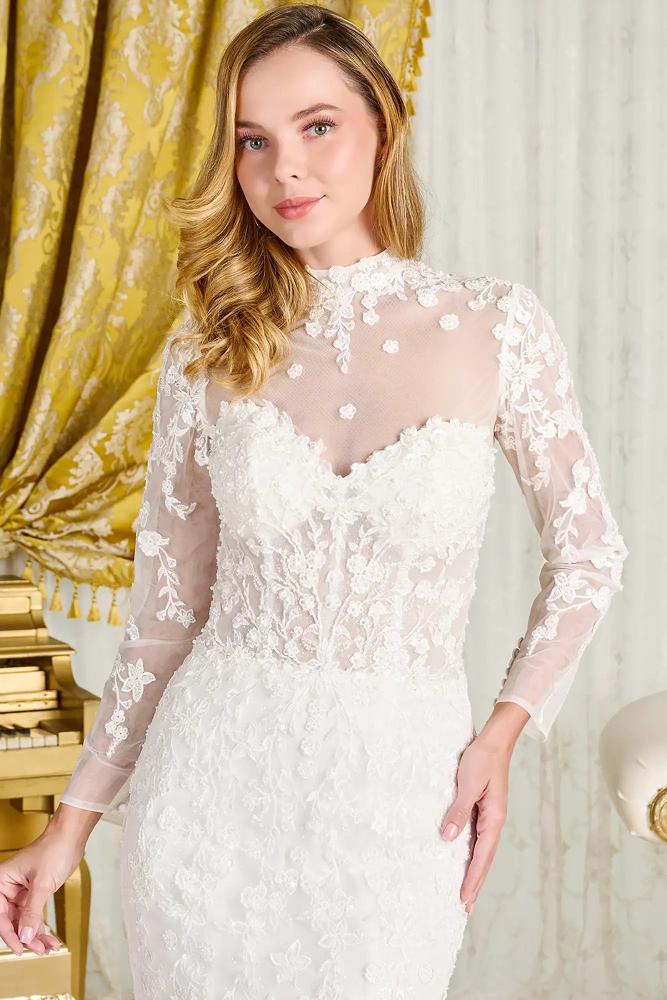 Woman wearing a white lace dress in a decorative room with gold curtains.