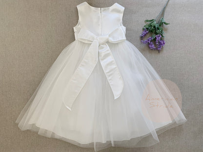 White flower girl dress with a large bow on a beige background