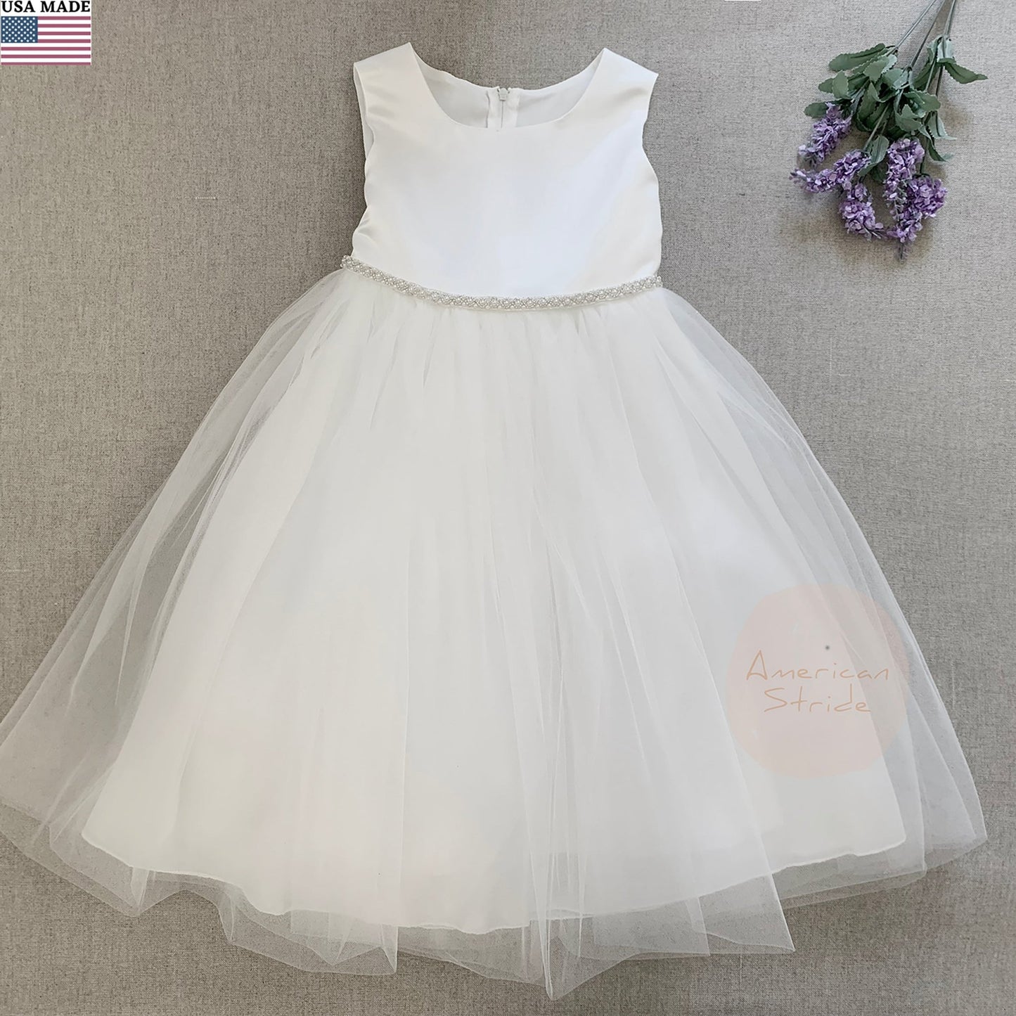 White flower girl dress with a sheer skirt on a gray background