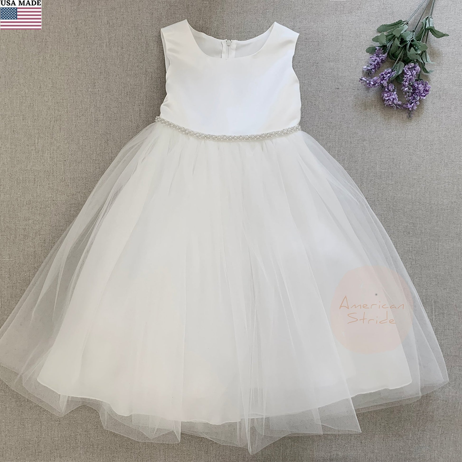 White flower girl dress with a sheer skirt on a gray background