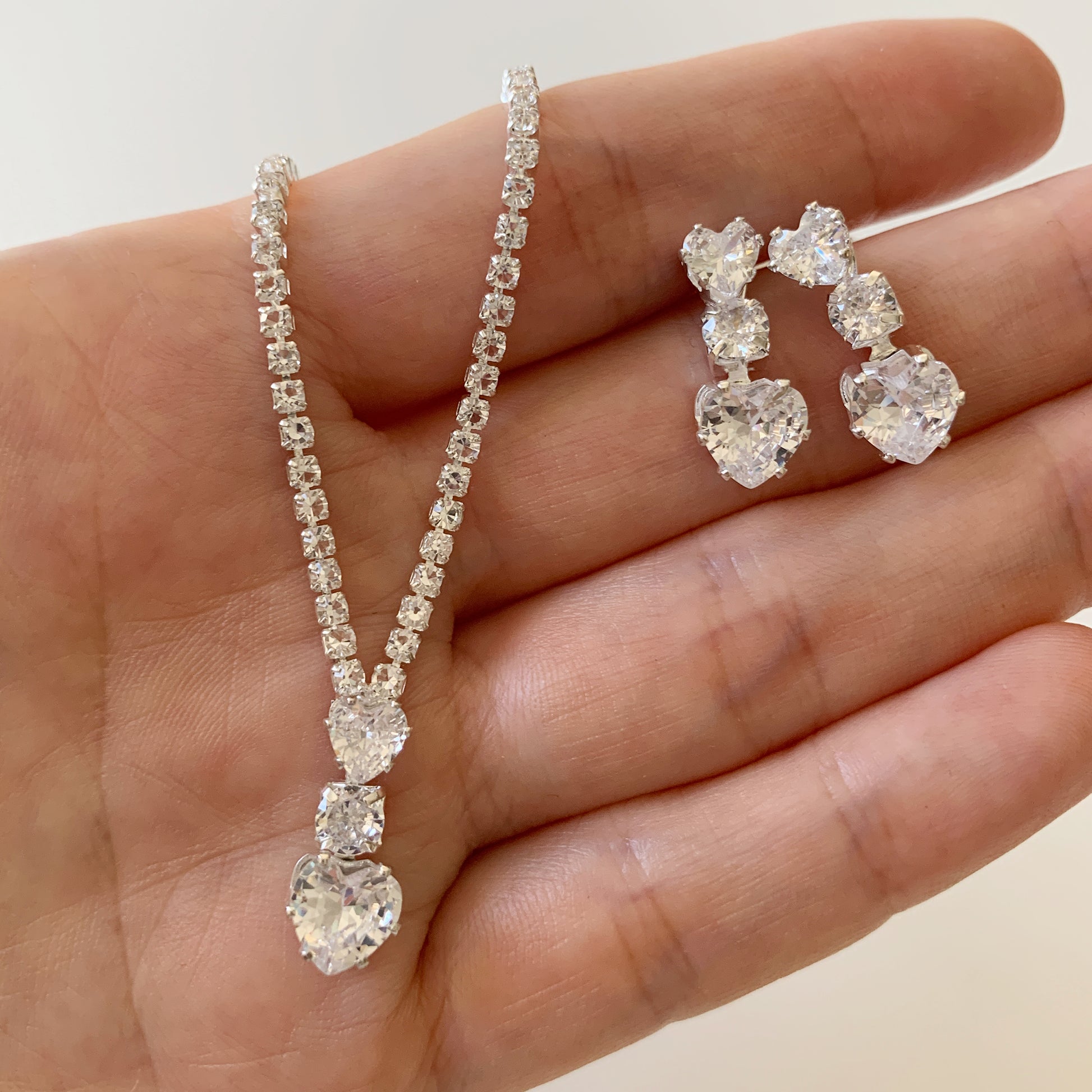 full rhinestone necklace and earrings held in a hand against a neutral background