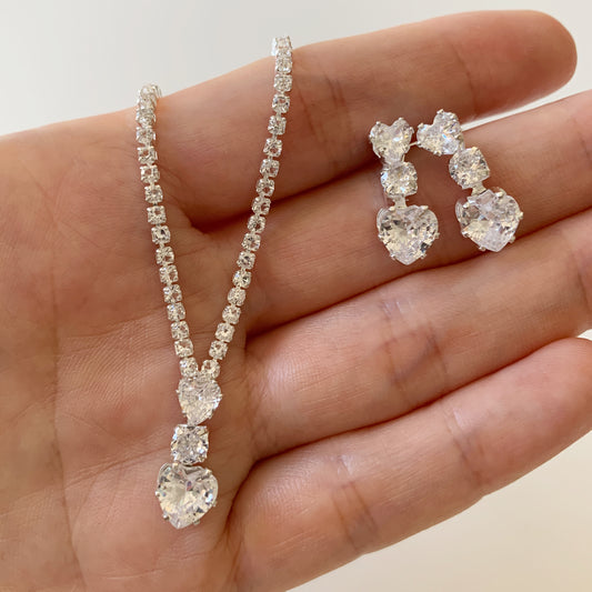 full rhinestone necklace and earrings held in a hand against a neutral background