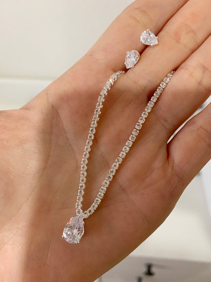 rhinestone necklace and earrings on a hand against a neutral background