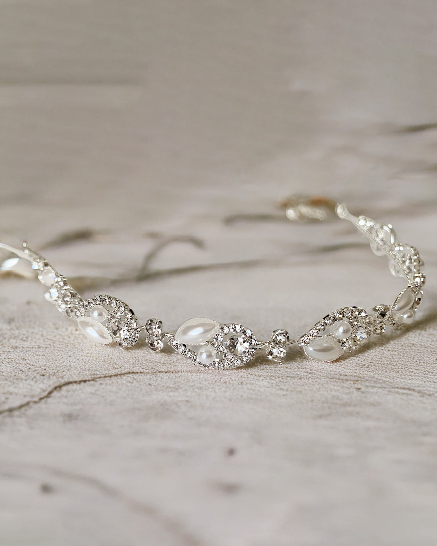 Silver bridal headpiece with pearls and crystals on a textured surface