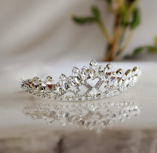 Silver tiara with clear gemstones on a reflective surface