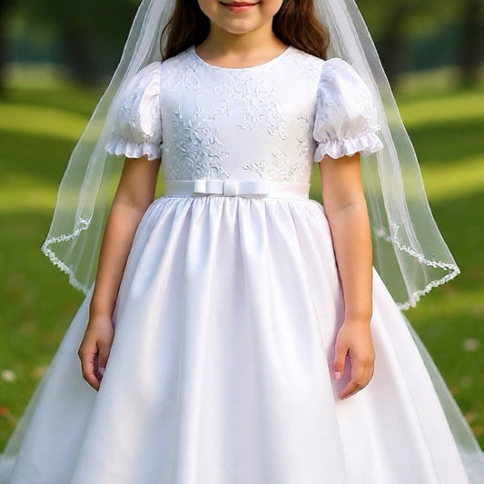 Young girl wearing a white dress with a veil against a green outdoor background