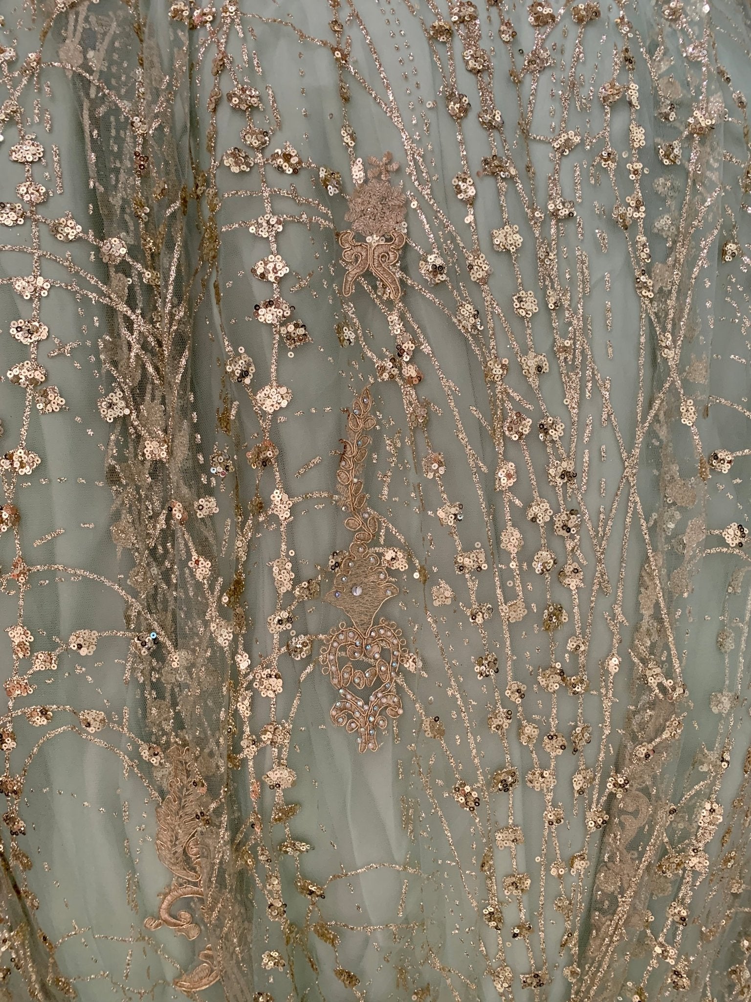 Close-up of a textured fabric with floral patterns and metallic accents on a light blue background.
