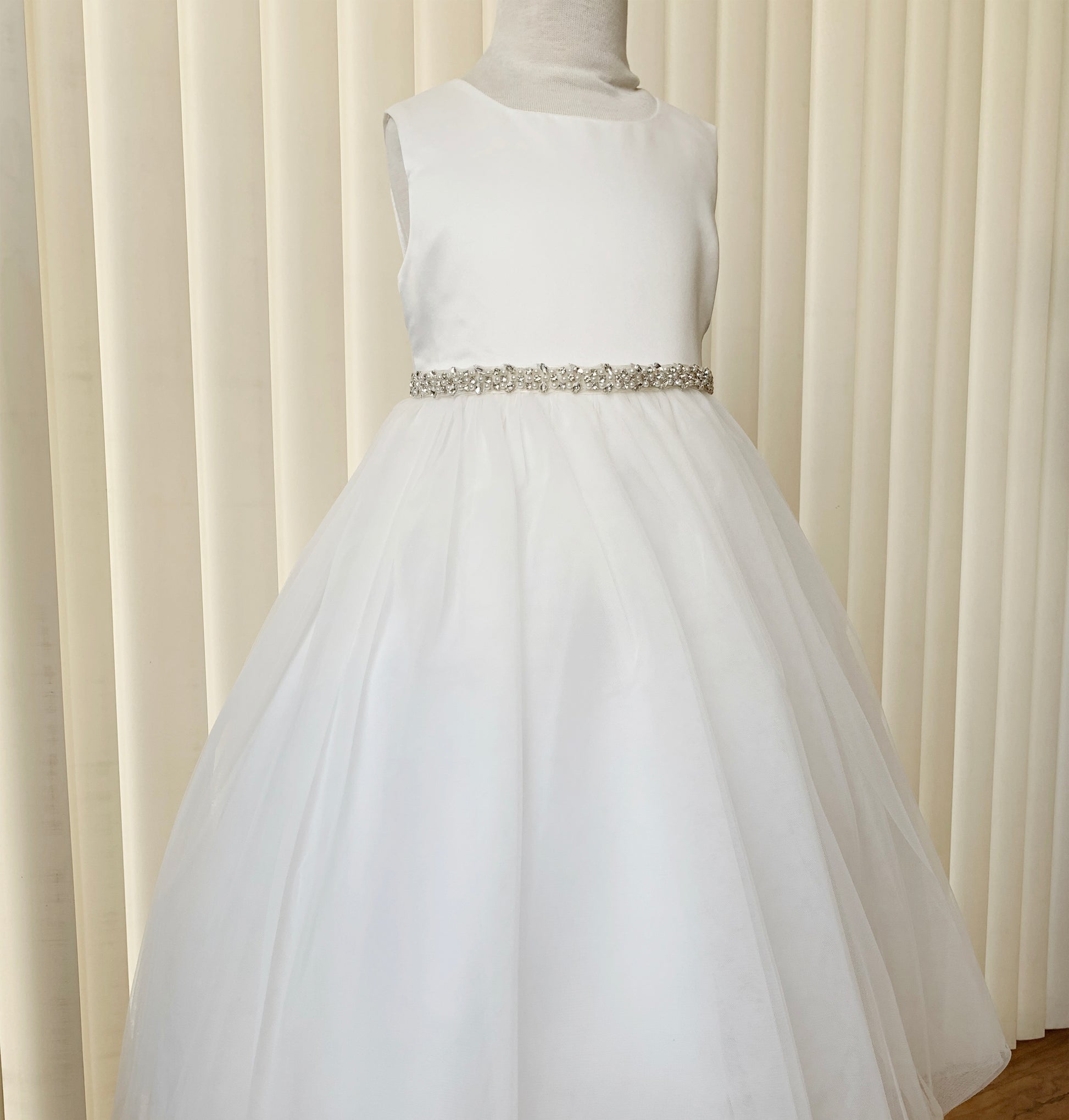 White dress with a silver belt on a mannequin against a beige curtain background