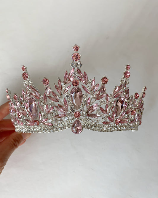 Pink and silver tiara held by a hand against a plain background