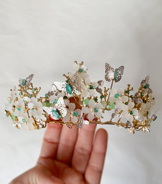 Floral tiara with butterflies held by a hand against a neutral background