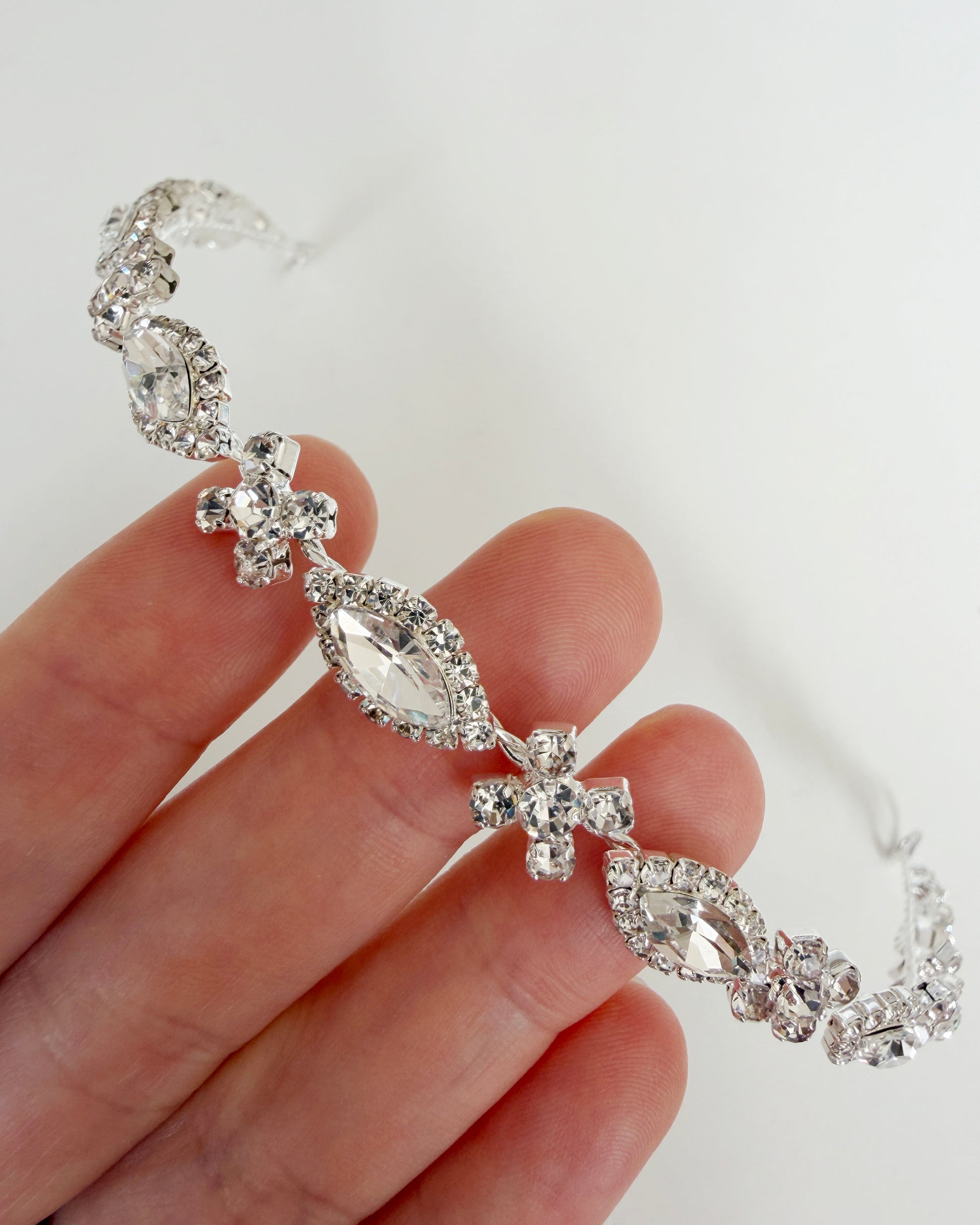 Silver jeweled headpiece held by a hand against a white background