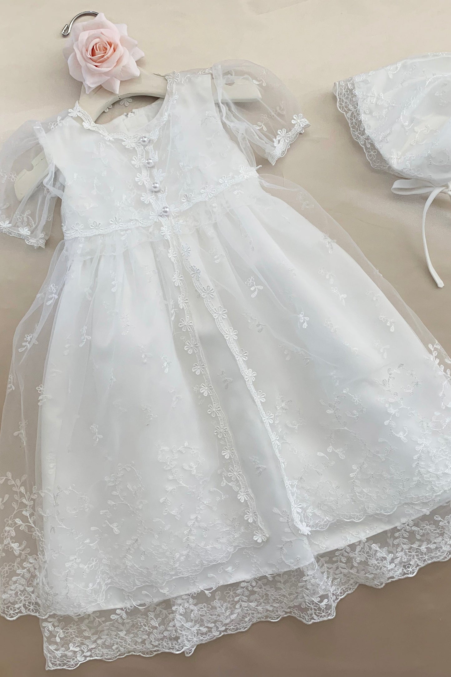 White baby baptism tulle dress with matching bonnet on a beige background