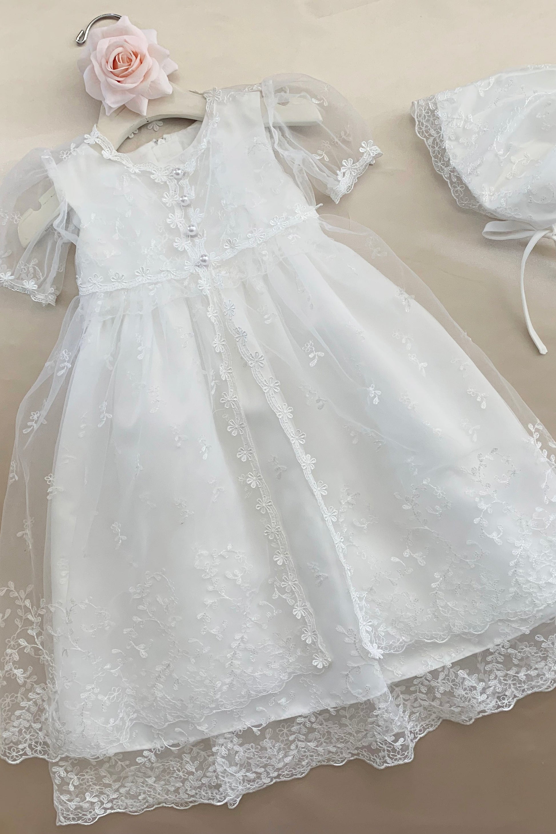 White baby baptism tulle dress with matching bonnet on a beige background