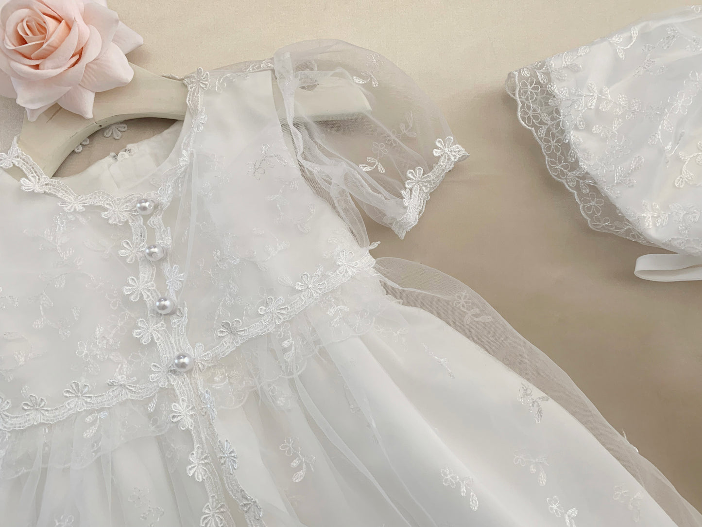 White baby baptism tulle dress with floral embroidery on a beige background