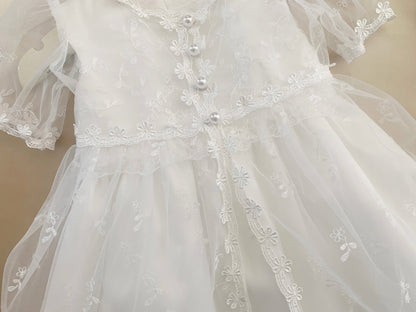 White baby baptism tulle dress with floral embroidery on a plain background