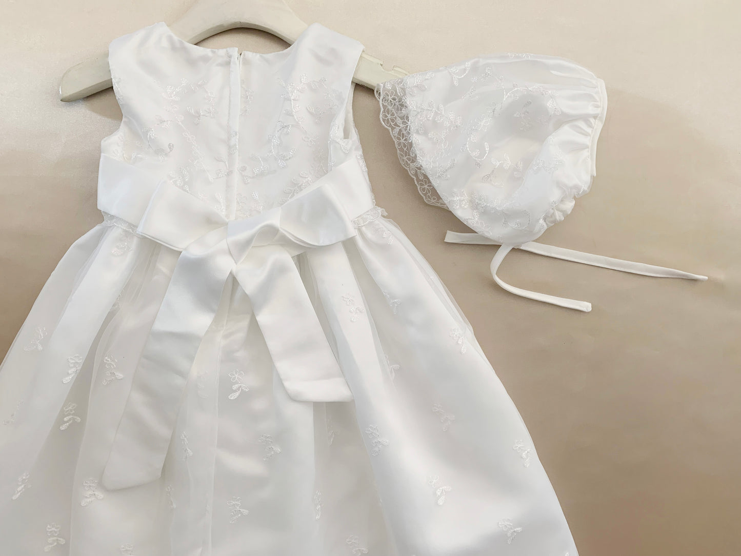 White baby baptism tulle dress with matching bonnet on a beige background