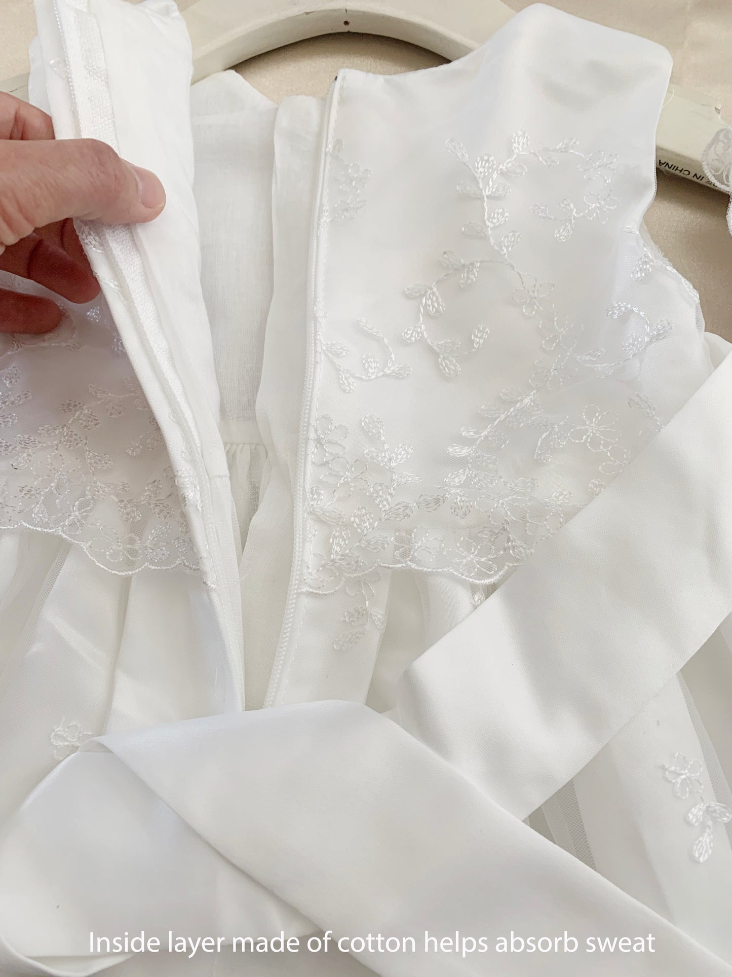 White baby baptism tulle dress with a hand holding it, showing the inside layer made of cotton.