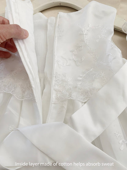 White baby baptism tulle dress with a hand holding it, showing the inside layer made of cotton.