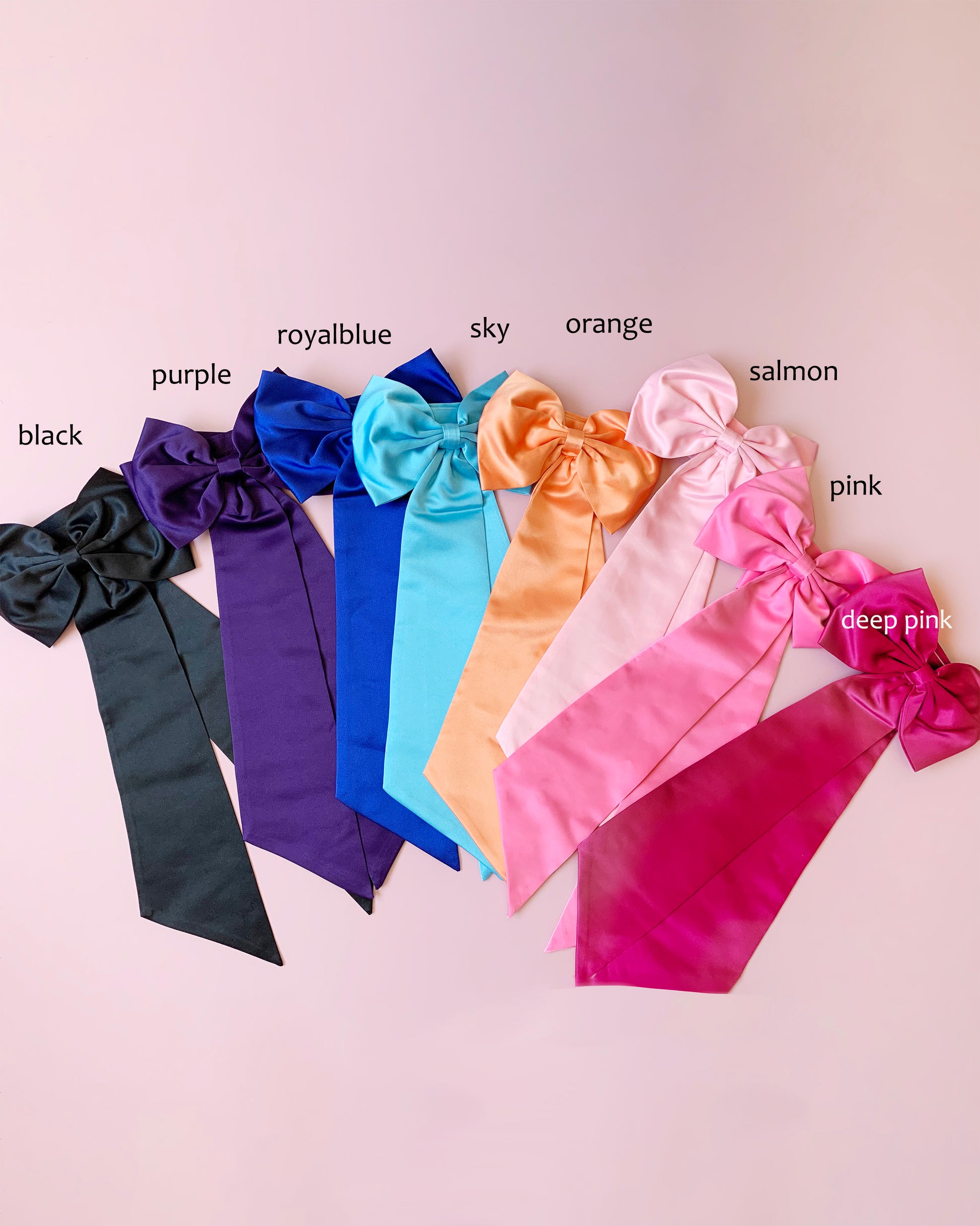 Set of colorful satin ribbons with labeled colors on a light pink background