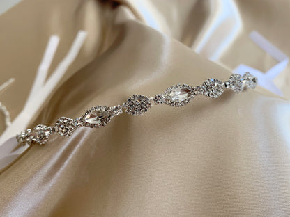 Silver jewelry piece with crystals on a beige fabric background