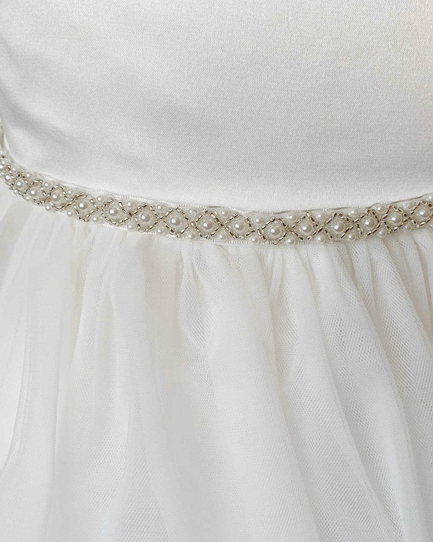Close-up of an off white dress with a decorative ivory belt featuring pearls and crystals.