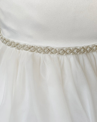 Close-up of an off white dress with a decorative ivory belt featuring pearls and crystals.