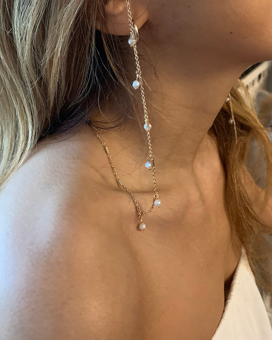 Close-up of a delicate eyewear necklace with small pearls on a person's neck.