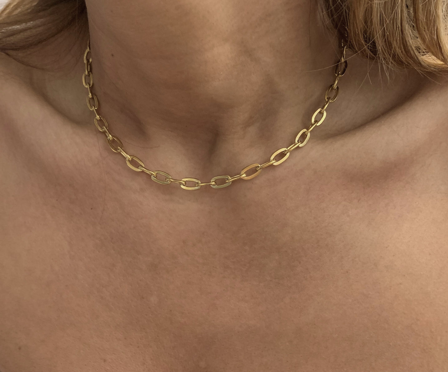 Gold chain necklace on a person's neck with a neutral background
