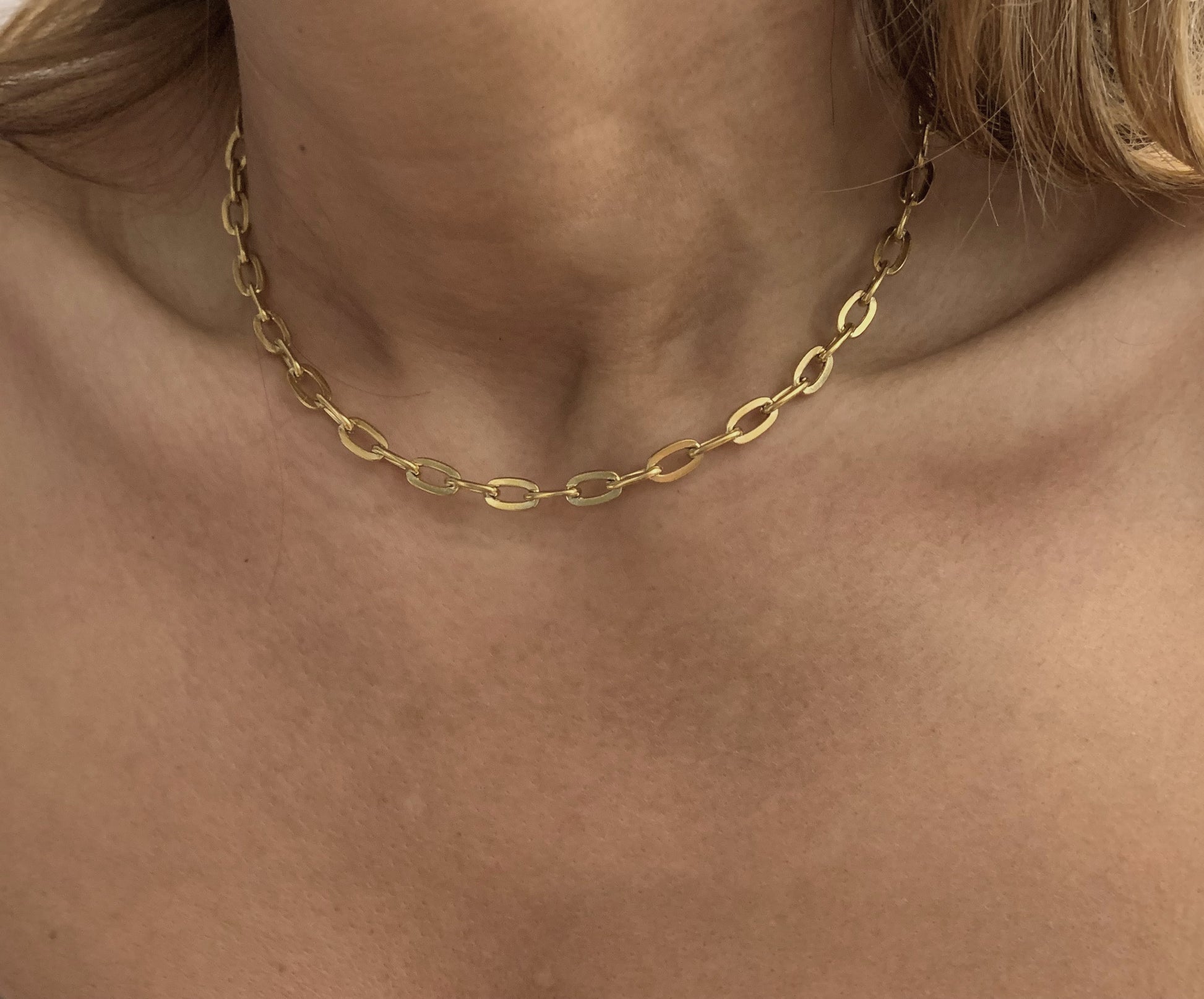 Gold chain necklace on a person's neck with a neutral background