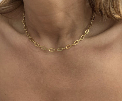 Gold chain necklace on a person's neck with a neutral background