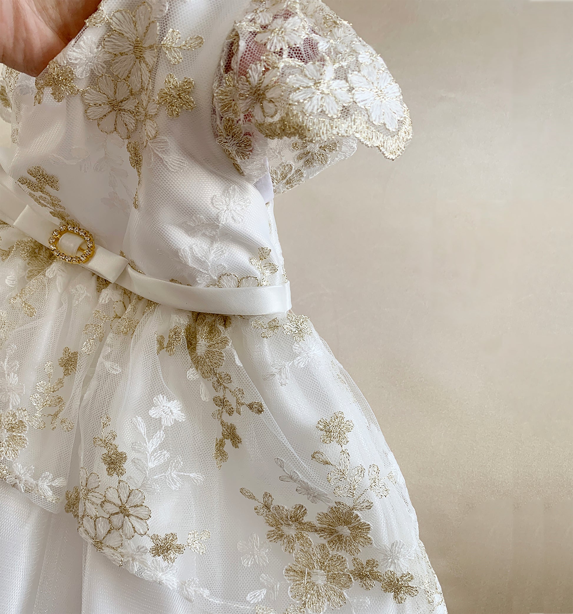 White lace dress with gold embroidery on a beige background