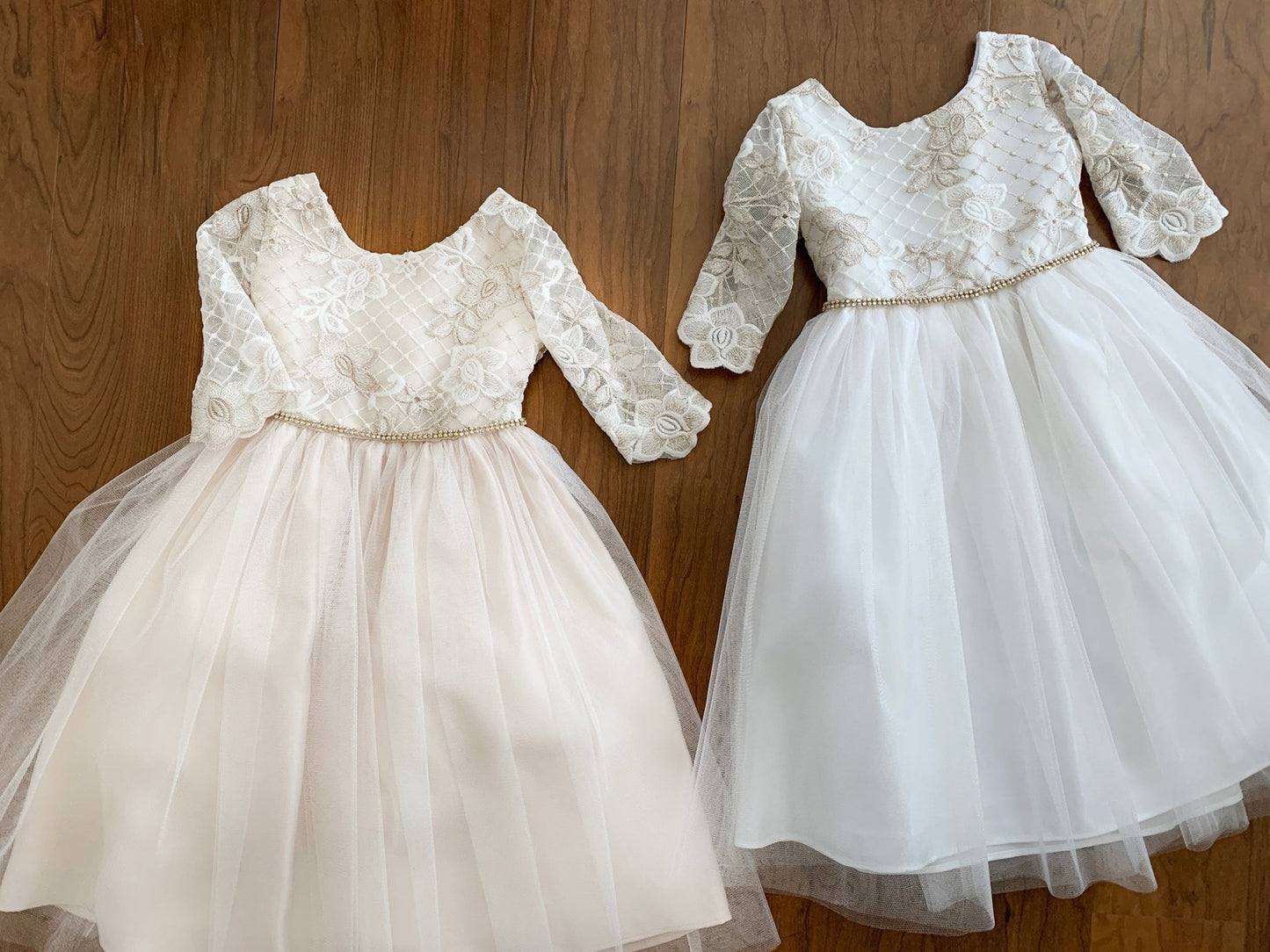 Two white lace dresses with long sleeves on a wooden surface